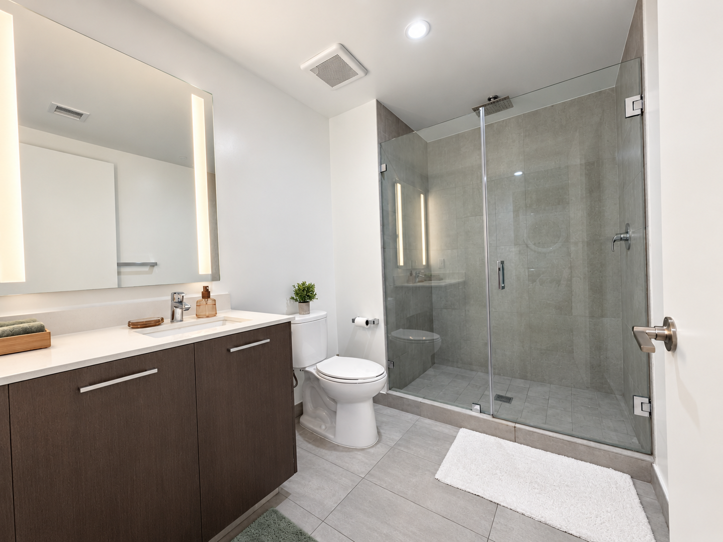 The bathroom of Unit 1402, with a walk-in glass shower and backlit mirror