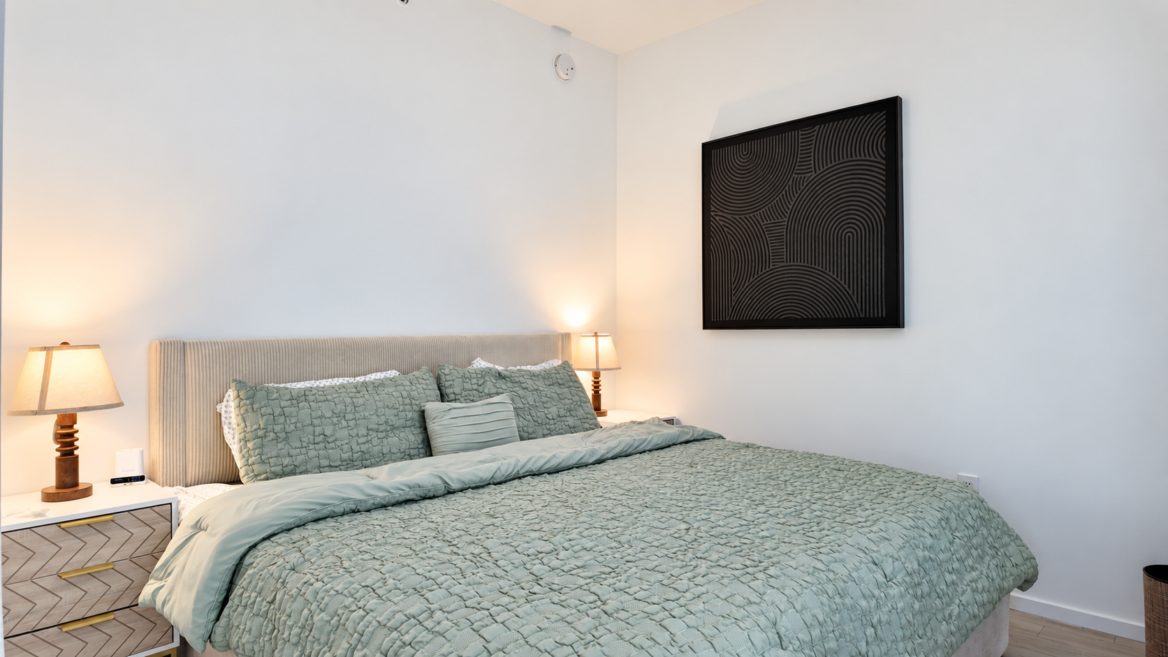 The bedroom of Unit 1402, with sage-green bedding and warm bedside lamps